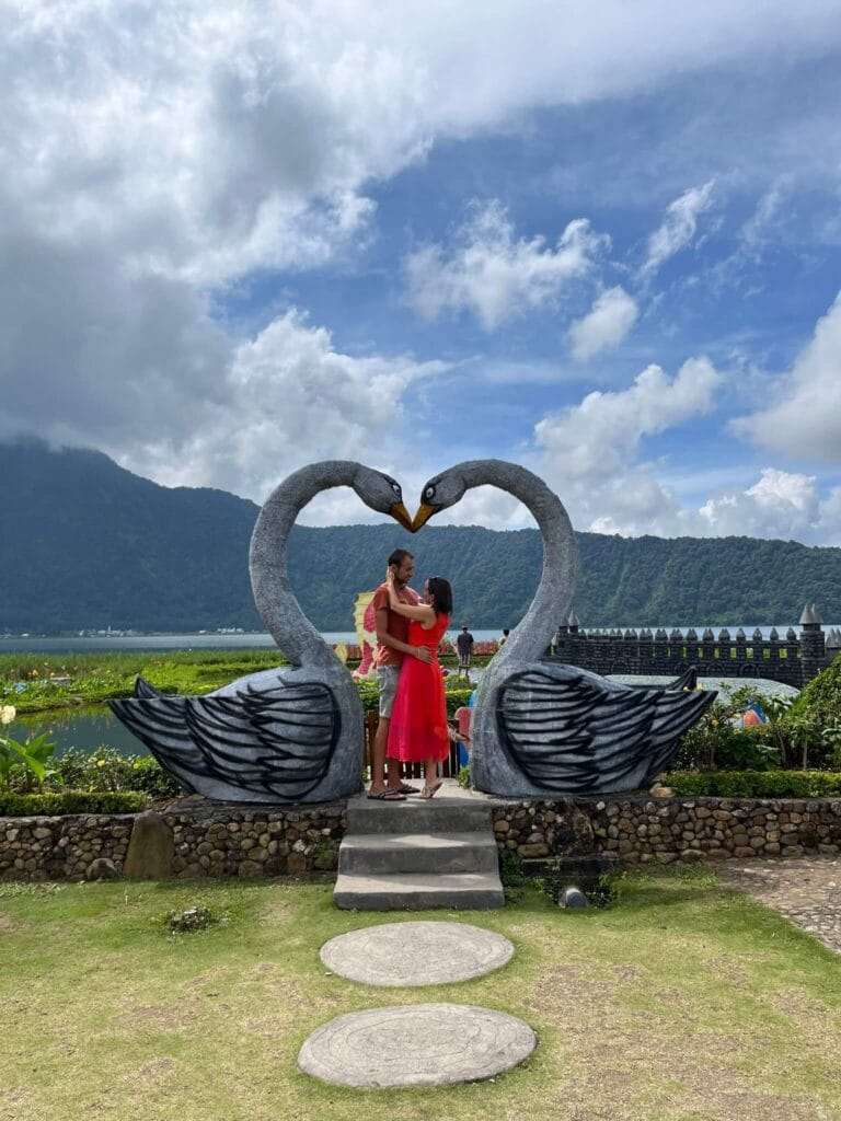 Travel couple standing at swan heart statue viewpoint in Bedugul with mountains in the background, Bali