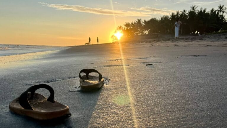 Sandals left on Canggu Beach at sunrise with golden sunlight reflecting on the sand in Bali