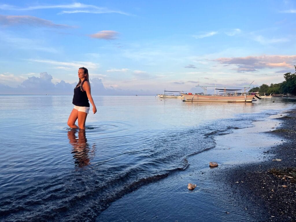 Traveler walking along the calm black sand beach of Lovina at sunrise in North Bali